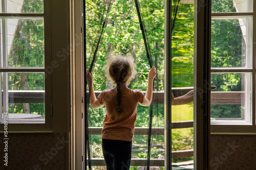 Magnetic mosquito net mesh on balcony door. Child going outdoors to home balcony through, preventing insects coming inside.