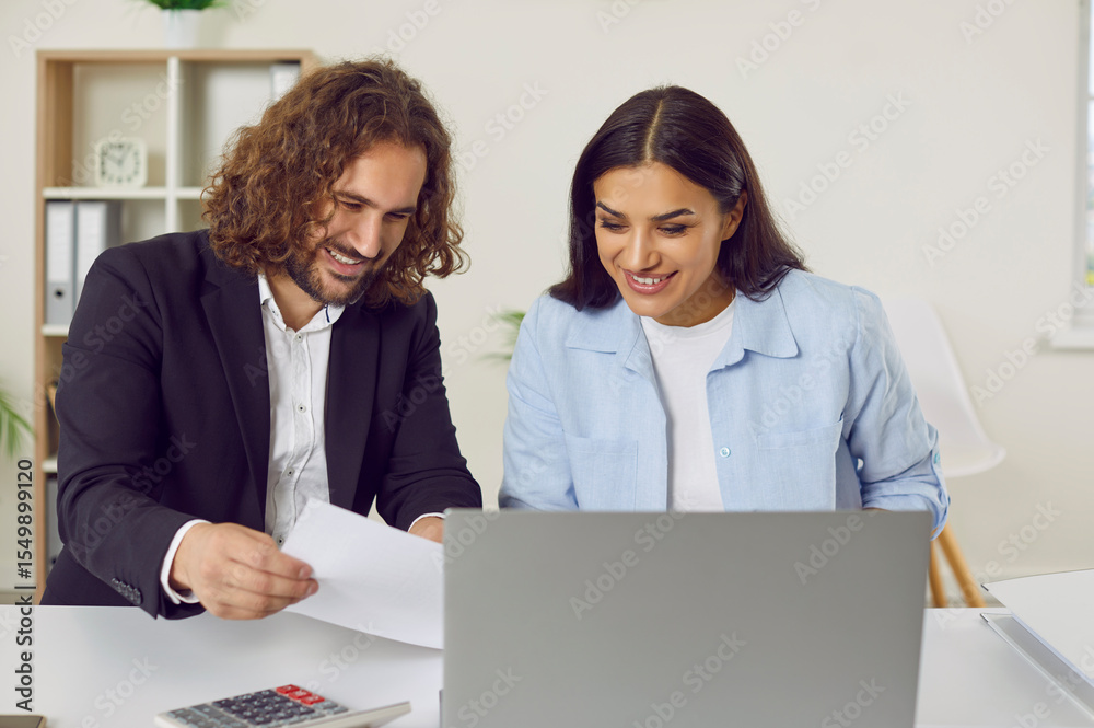 Fototapeta premium Male accountant or auditor meeting with female client. Two happy people sitting at office desk and working with some business documents. Young man and woman looking through papers at table with laptop