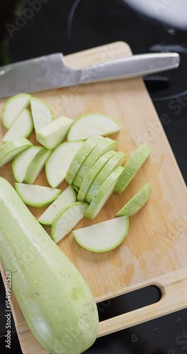 Vertical slow-motion footage of slices of sliced zucchini are on the cutting board on the kitchen table, a kitchen knife