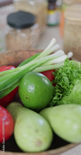 Vertical slow-motion footage of plate with broccoli, green onion, red radish, lettuce, pomegranate, tomatoes and avocado, next to jars of spices and cereals