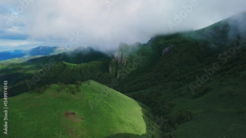 Breathtaking aerial view of green mountains and dramatic clouds in early morning light. Mount Chertovy Vorota in Adyghea, drone shot