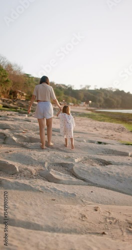 Mother walking with her daughter on ocean coastline. Family and sunset sunshine
