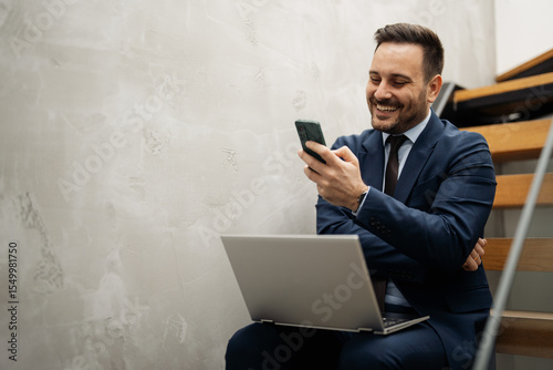 Businessman sitting on stairs and using laptop and smartphone
