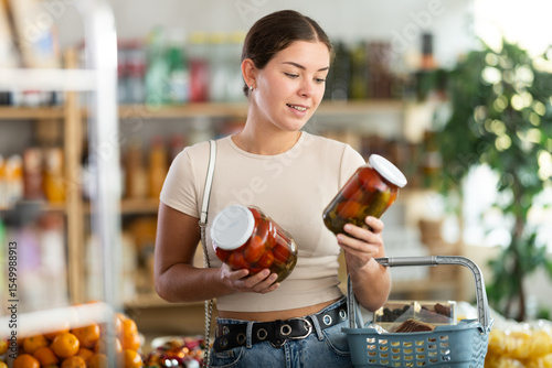 Woman looking at pickled tomatoes in store. Market visitor choose consider jar with pickled tomato cucumbers. Buyer pick up set of groceries, consider available options