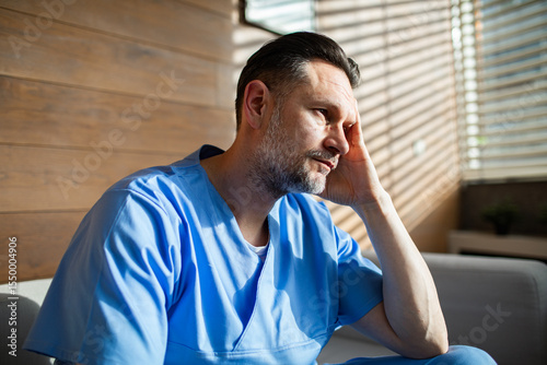 Tired male healthcare worker sitting on couch and resting after long shift