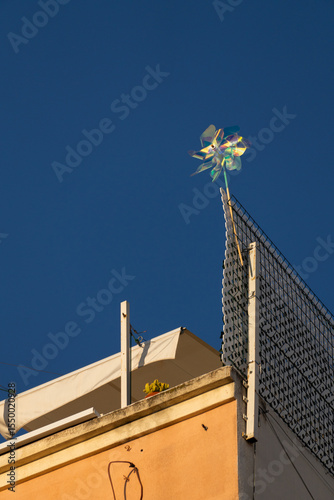 A vibrant pinwheel spinning atop a rooftop structure with a deep blue sky in the background. The photo captures a playful detail in an urban setting.