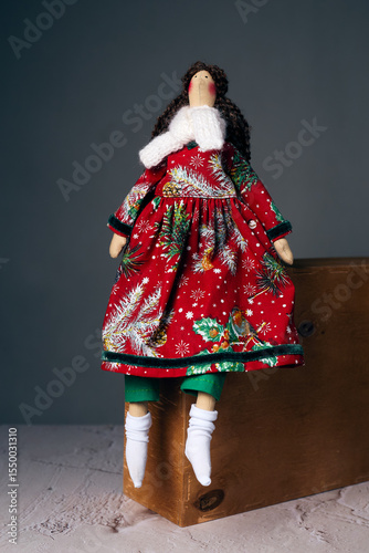Handmade textile doll in red Christmas dress sitting on wooden box indoors