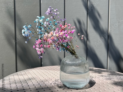 Colorful gypsophila bouquet in a ribbed glass vase on a perforated table lit by soft natural light and shadows