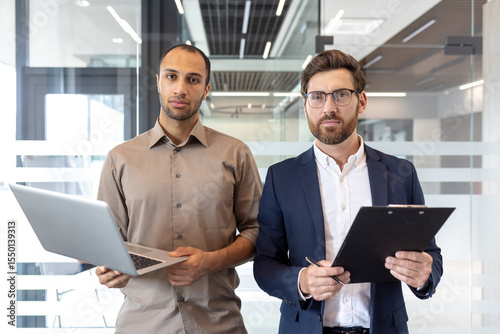 Two diverse business professionals standing confidently in a modern office setting, ready for business.