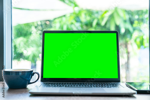 Mockup of laptop computer with empty screen with coffee cup and smartphone on table of the coffee shop background,Green screen