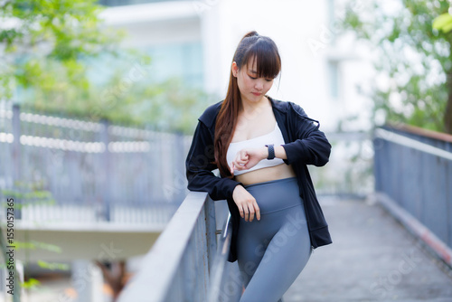 Portrait of beautiful asian Young woman in Black robe sportswear working out outside. training on public equipment Watching the Smart Watch in outdoor at park. concept Exercise Healthy lifestyle.