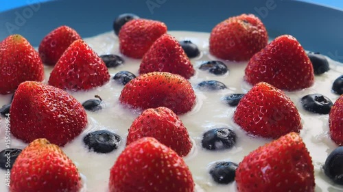 Strawberries and blueberries ripe berries in heavy cream rotating in a circle on a blue background. Medium shot.