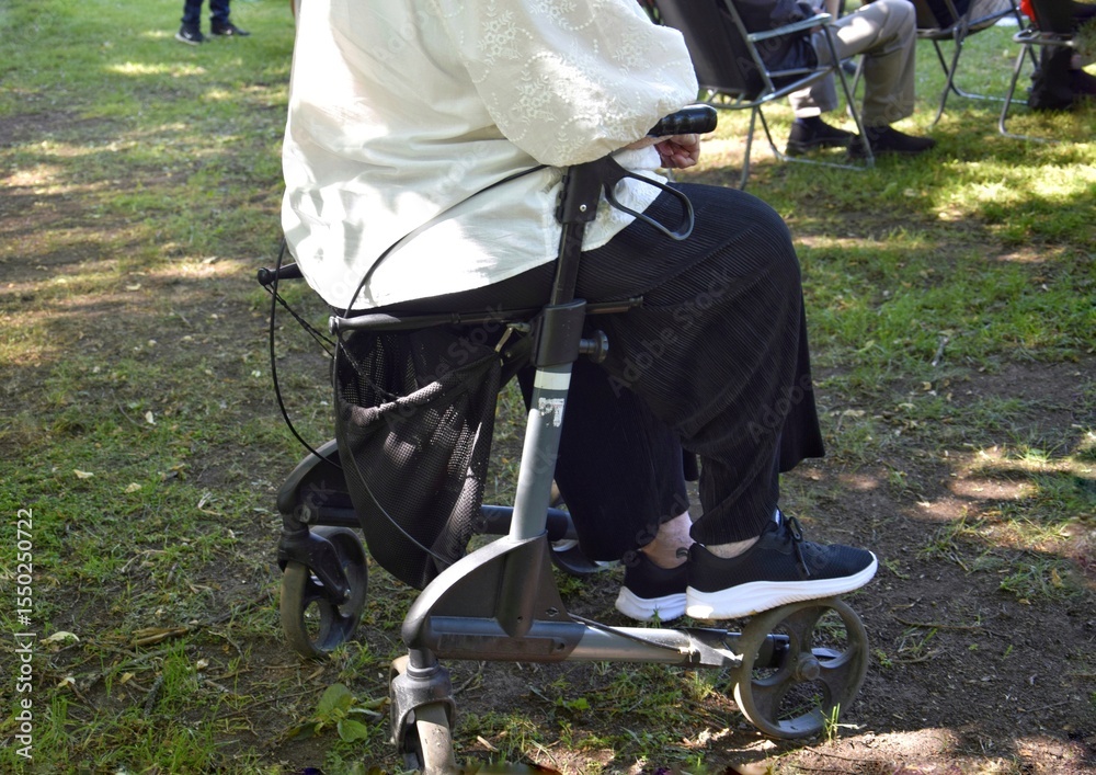 Obraz premium An elderly woman sits on the seat of her walker in the shade.