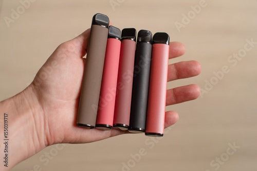 Various disposable electronic cigarettes in a female hand on a light background