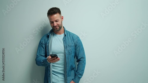 Portrait of happy casual man using phone, Young guy standing at white wall, smiling, Isolated on white background, blank copy space.