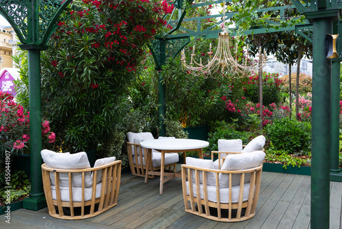A cozy outdoor seating area with four rattan chairs and a round table surrounded by lush green plants and vibrant flowers