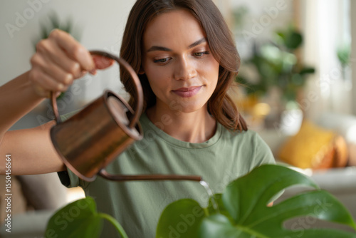Woman watering monstera plant with copper watering can at home photo