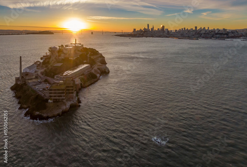 Alcatraz Island, a former prison, sits in the San Francisco Bay, USA, at sunset. The city skyline and the Bay Bridge are visible in the background.