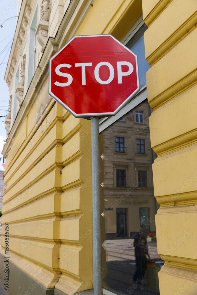 Prominent Stop Sign in Front of a Calm Yellow Building with Reflection, Signifying Caution and Attention Needed for Passing Vehicles or Pedestrians Nearby Prominent Stop Sign in Front of a Calm Yellow Building with Reflection, Signifying Caution and Attention Needed for Passing Vehicles or Pedestrians Nearby