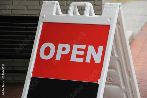 Open sign with white letters on red background at the entrance of a business using an A frame which can be seen from different angles to attract foot traffic.