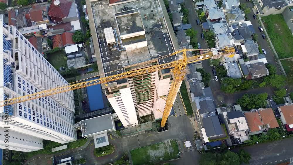 Aerial shot of a construction site in Jakarta, Indonesia. Features a tall building under construction with a yellow crane, surrounded by houses and apartment buildings. Camera moves slowly.