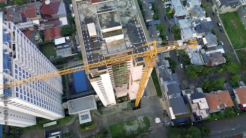 Aerial shot of a construction site in Jakarta, Indonesia. Features a tall building under construction with a yellow crane, surrounded by houses and apartment buildings. Camera moves slowly.