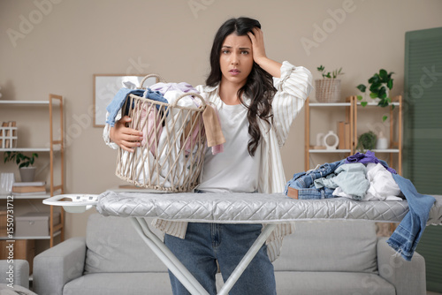 Tired young woman with dirty laundry and ironing board at home. Stress concept