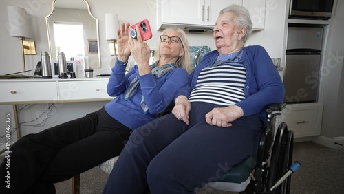A daughter shares joyful moments with her elderly mother using a smartphone while seated comfortably indoors, showcasing their connection and care for each other.