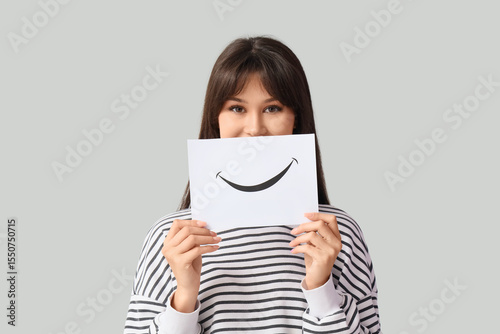 Young woman with paper smile on light background