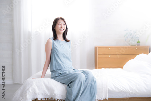 寝起きでベッドに座る女性の全身の広角　爽やかな朝のスッキリ起きるイメージ