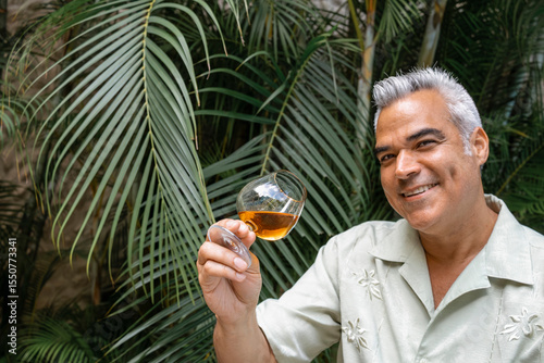 Portrait of Smiling mature man holding and tasting a glass of rum