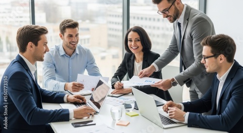 Diverse group of business professionals collaborating in a modern office meeting discussing reports and data on laptops and papers with bright natural light