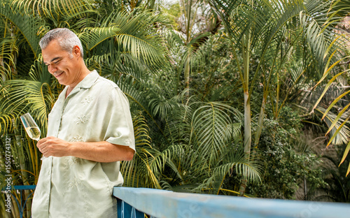 Mid adult man tasting sparkling wine in tropical garden