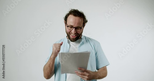 Man in a light blue shirt and glasses reacts happily to positive news he has received on paper. He is very excited and pleased with the information. Perfect for business, finance, good news concepts.
