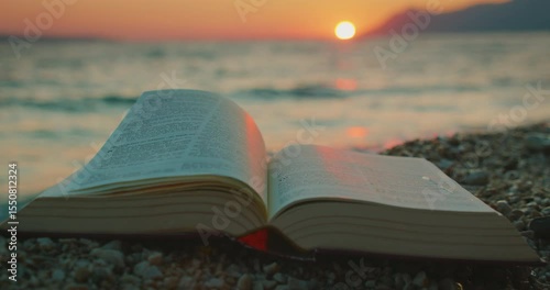 Open book Holy Bible on a pebble beach at sunset with sea waves in background