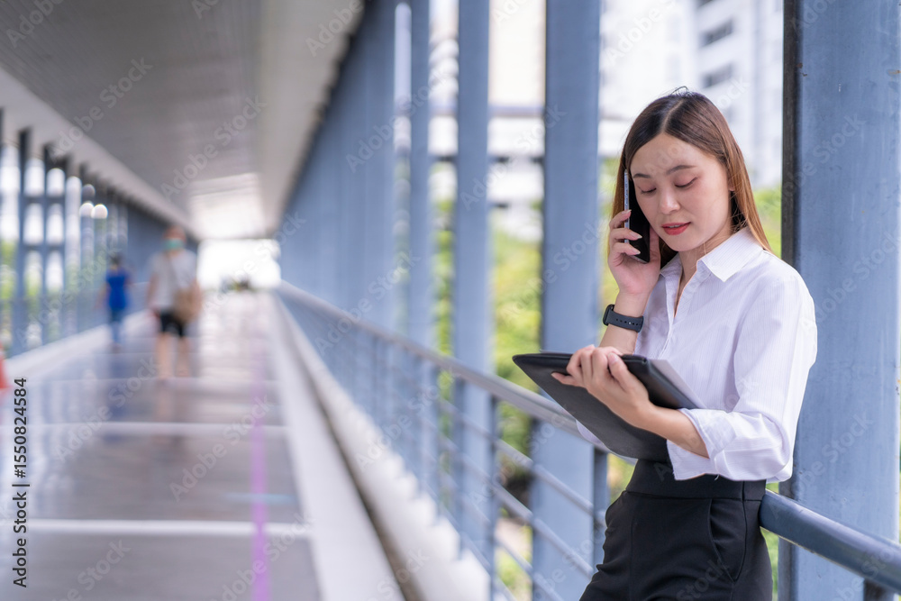 Fototapeta premium A woman is talking on her cell phone while looking at a tablet