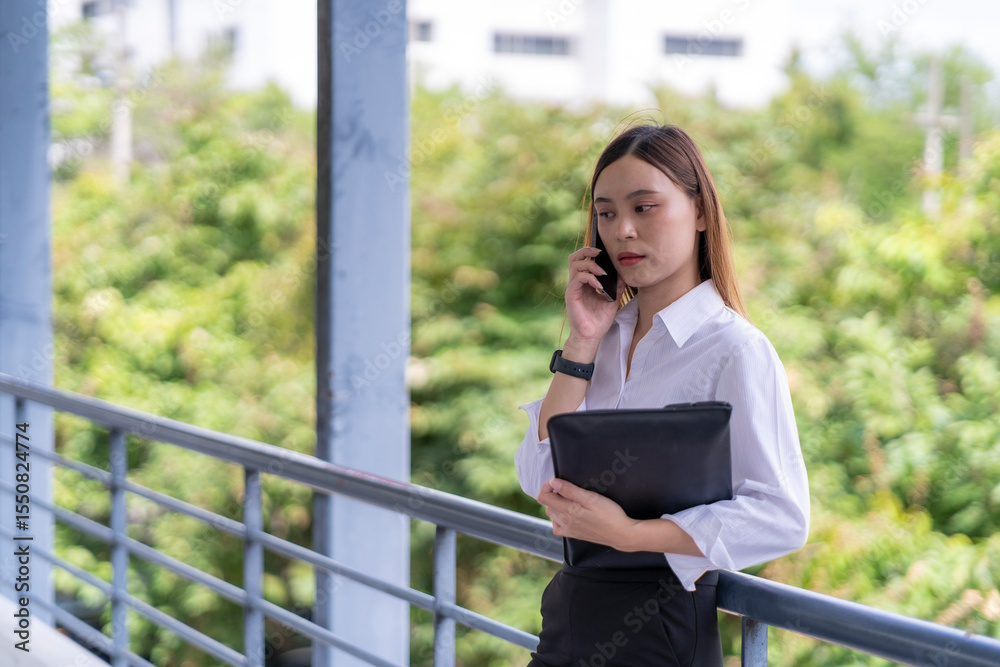 Fototapeta premium A woman is talking on her cell phone while holding a black purse
