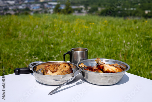A tourist's picnic lunch. Two metal plates with smoked lard and chicken meat stand on the table next to a mug with a drink.
