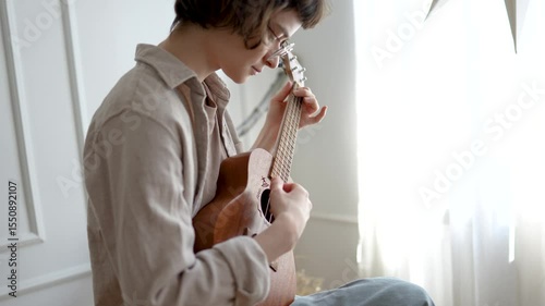Engaged woman playing ukulele, strumming strings and pressing frets to learn chords and rhythms. Musical practice, instrument exploration, musician creative melodic discovery and coordination