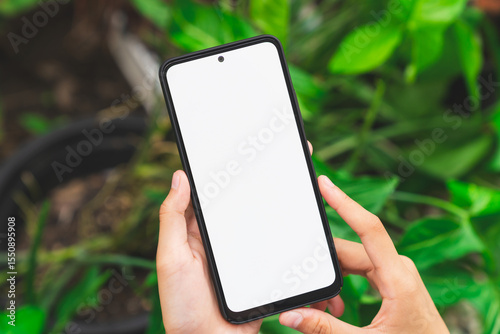 Hand holding smartphone with blank screen for graphic display montage on outdoors background, mockup display for lifestyle and wireless technology.