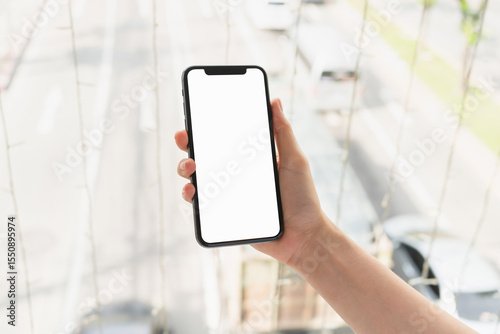 Hand holding smartphone with blank screen for graphic display montage on outdoors background, mockup display for lifestyle and wireless technology.