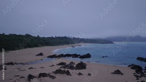 Flying over breaking waves on deserted sand beach with foggy coastline