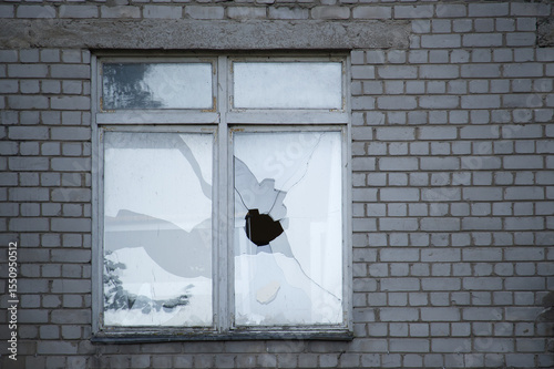 A broken window with shattered glass in an old brick wall evokes a sense of urban decay.