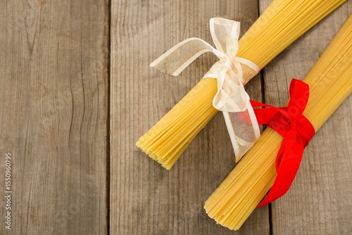 Raw spaghetti tied with ribbons on wooden table