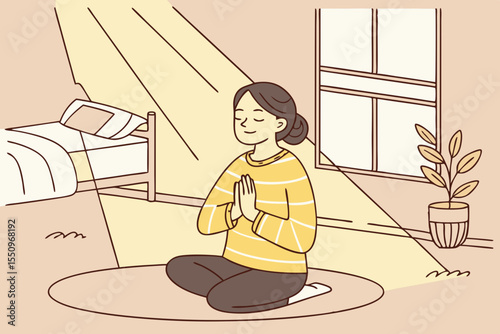 A woman sits cross legged on the floor of a cozy, sunlight filled bedroom at home, meditating in a yoga pose. She is calm and relaxed, wearing a striped yellow sweater