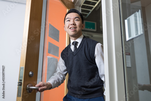 A young man in business attire opens a door and walks confidently into a room, suitable for themes like job interviews, office culture, internships, or first day of work scenarios.