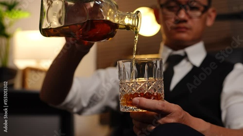 Businessman holding a glass of whiskey, sitting and drinking in a room