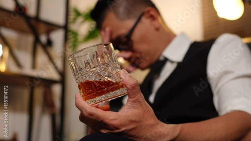 Businessman holding a glass of whiskey, sitting and drinking in a room