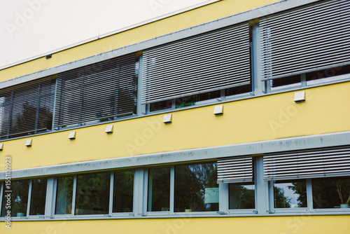 This modern building features a bold yellow facade with stylish window blinds, exemplifying contemporary design and capturing the essence of modernism in architecture and aesthetics
