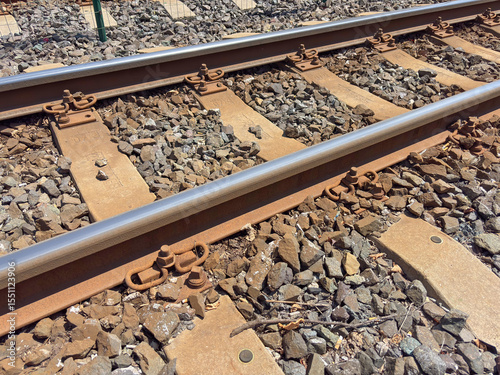 Close up of train tracks with metal rails, wooden sleepers, and gravel ballast under sunny conditions, concept of transportation, infrastructure, travel.